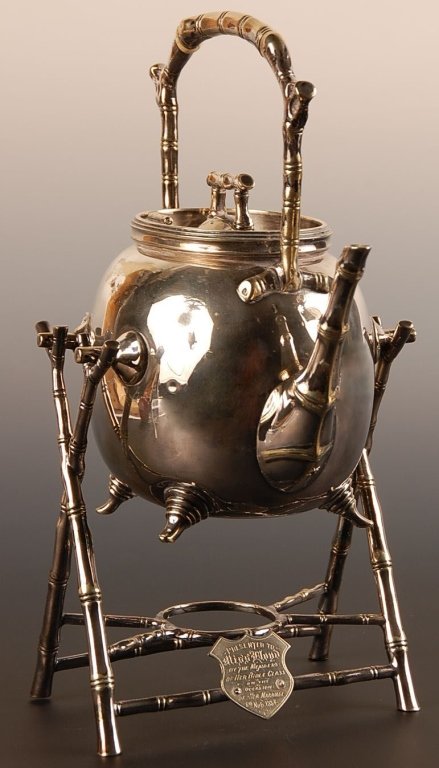 1886 JAPANESQUE TIPPING TEA KETTLE ON STAND: Silver plated teapot rests in a bamboo motif stand, the presentation plaque on the base reads 'Presented to Miss Lloyd by the members of her Bible class on the occasion of her marriage 9th Nov. 1886,'