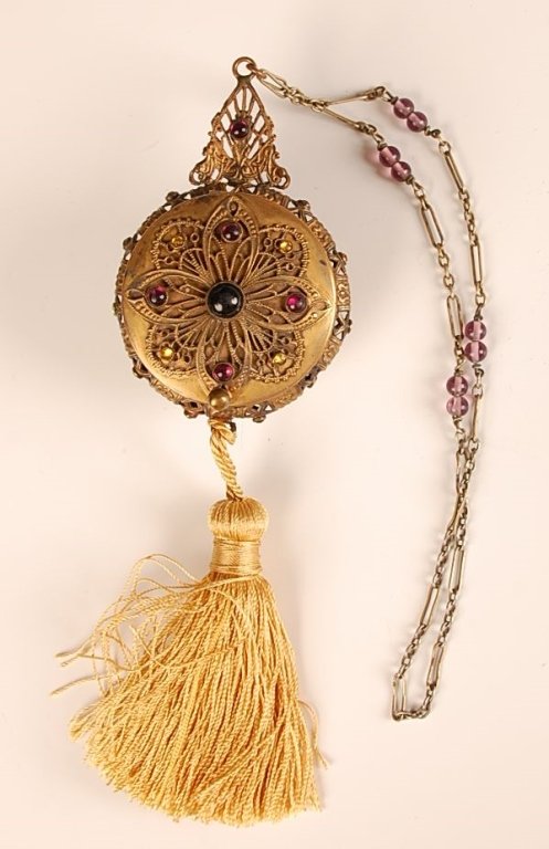 JEWELED FILIGREE DOUBLE-SIDED COMPACT: Long chain handle, cord tassel, jewels and filigree on both sides, one side holds a framed mirror in the lid, Veri-flat puff and partial pan, the other side holds a satin gathered purse in the lid, po