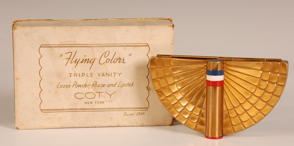 COTY 'FLYING COLORS' VANITY CASE WITH ORIGINAL BOX: Half round compact with wings design around lipstick in the top, mirror in the lid, base holds rouge well with branded puff and pan and hinged powder well with branded puff, marked on the bottom, meas