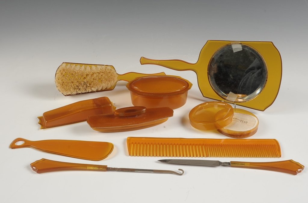 MARINELLO VINTAGE PLASTIC TEN PIECE VANITY SET: Amber plastic vanity set with a hairbrush, hand mirror with some silvering loss and the mirror is loose in it's frame, lidded soap dish, lidded toothbrush(?) holder, compact with branded puff, shoe ho