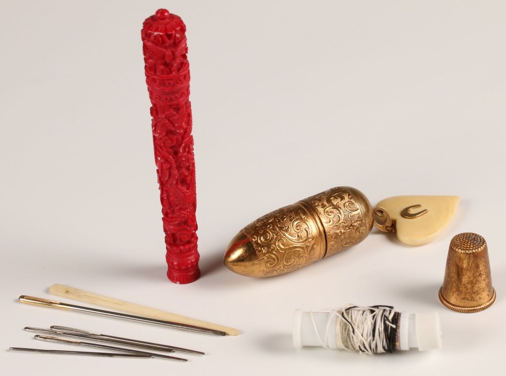 ANTIQUE THIMBLE AND NEEDLE CASES: A carved and stained bone needle case along with an embossed brass thimble case. Two pieces, with one red in color that measures 3.5 inches in length, and the other measures 2 inches in length.