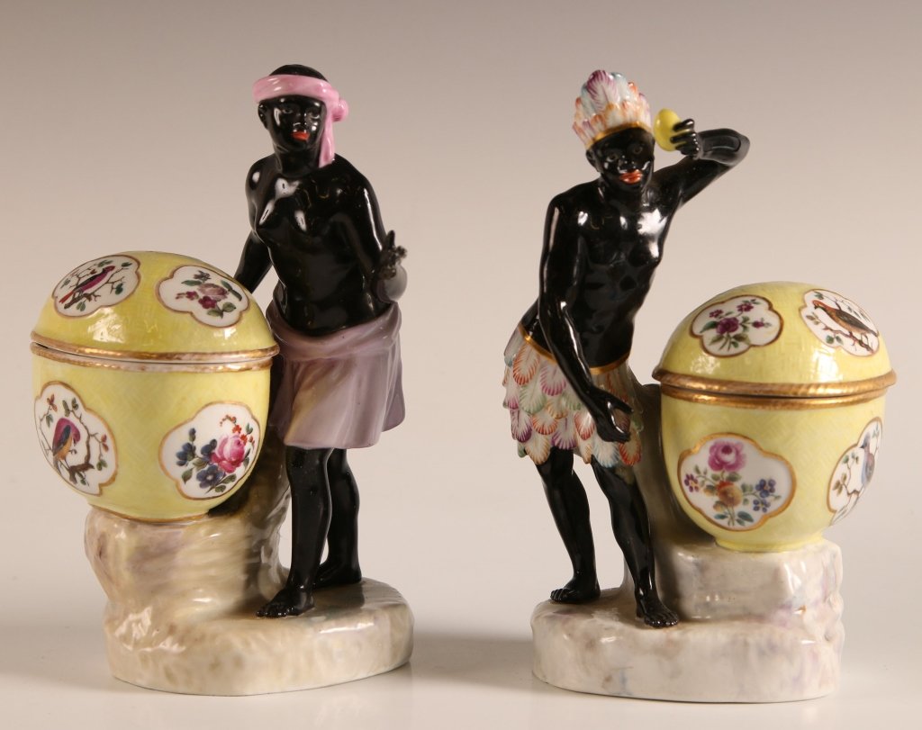 KPM PORCELAIN SWEET MEATS WITH BLACKAMOORS: A proper pair, each with male and female figures alongside a covered basket and standing on on a faux marbled rocky base; blue underglaze sceptre mark (covered by enamel glaze on one); repair to the f