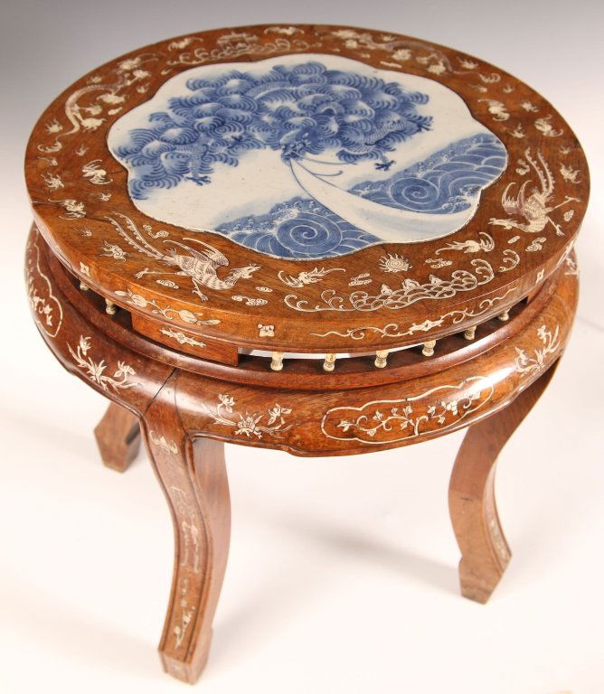 C. 1900 CHINESE HARDWOOD TABLE WITH PORCELAIN PLAQUE: Chinese, round export hardwood tea table having an inset scalloped-edge blue and white porcelain panel with a design of a dragon flying above stylized waves; the wood border adorned with inlays of aus