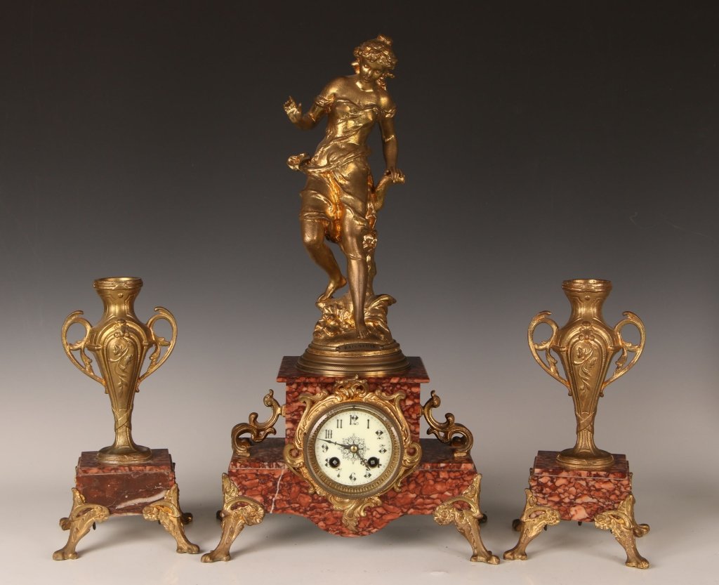 ANTIQUE FRENCH FIGURAL MANTLE CLOCK SET: Figural 'Baigneuse' on two step red marble clock, porcelain clock face with time and strike. Gilded furniture and legs. Unsigned. Measures 21 x 11.5 x 6.5 inches. Two similar style urns on marble base