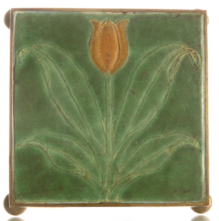 GRUEBY POTTERY TWO COLOR TILE: Mounted in a brass frame for use as a trivet. These tiles are typically unsigned. The reverse is marked with the letters D C, a decorator's marks. Measures 1.25 x 6.75 inches.
