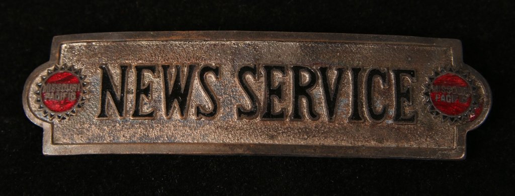 MISSOURI PACIFIC RAILROAD NEWS SERVICE CAP BADGE: Die struck with translucent red enamel Mo Pac logo roundels, enamel shows cracking; black enamel lettering, double screwback, 1 x 4 inches. Average - good condition.