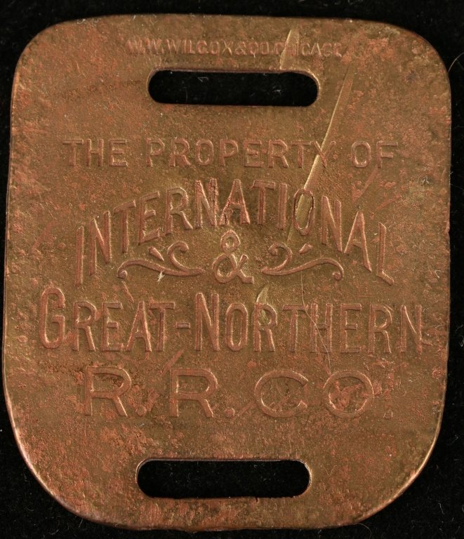INTERNATIONAL GREAT NORTHERN RAILROAD LUGGAGE TAG: Stamped brass with logo, W.W. Wilcox & Co. maker's mark, 2-1/4 x 1-7/8 inches, average condition.