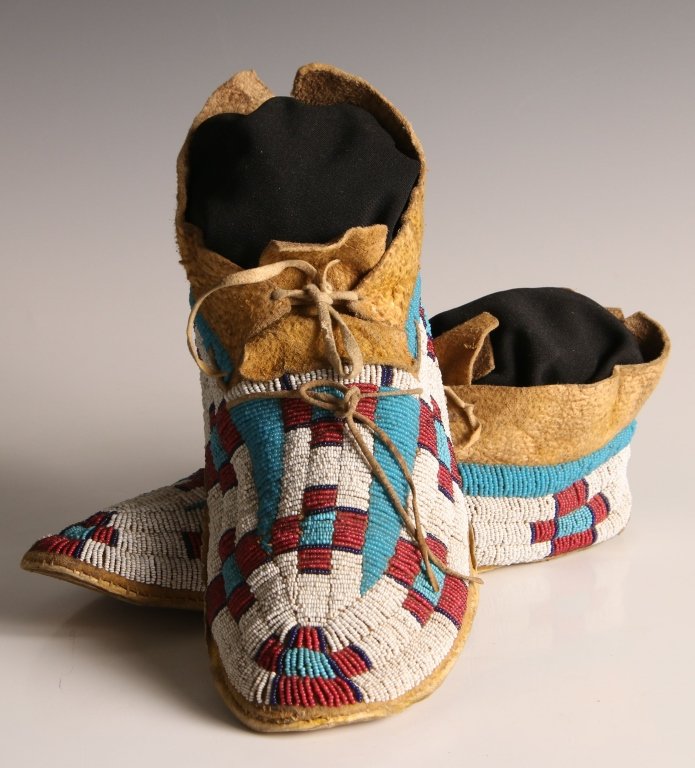 C.1900 RED, WHITE AND BLUE SIOUX BEADED MOCCASINS: Sioux moccasins; the pair dates to circa 1900; the uppers are fully beaded with red and blue crosses and light blue "buffalo track" designs on a white background. Measure 3.5 x 9.5 x 3 inches each.
