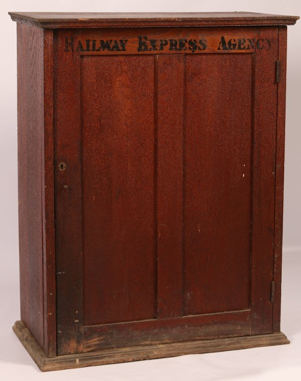 RAILWAY EXPRESS AGENCY TICKET CABINET: An ash wood cabinet with black stenciled lettering on the paneled front door, a divided interior and labels on the inside of the swing door with a date of August 18, 1932. On the left side is a tin ta