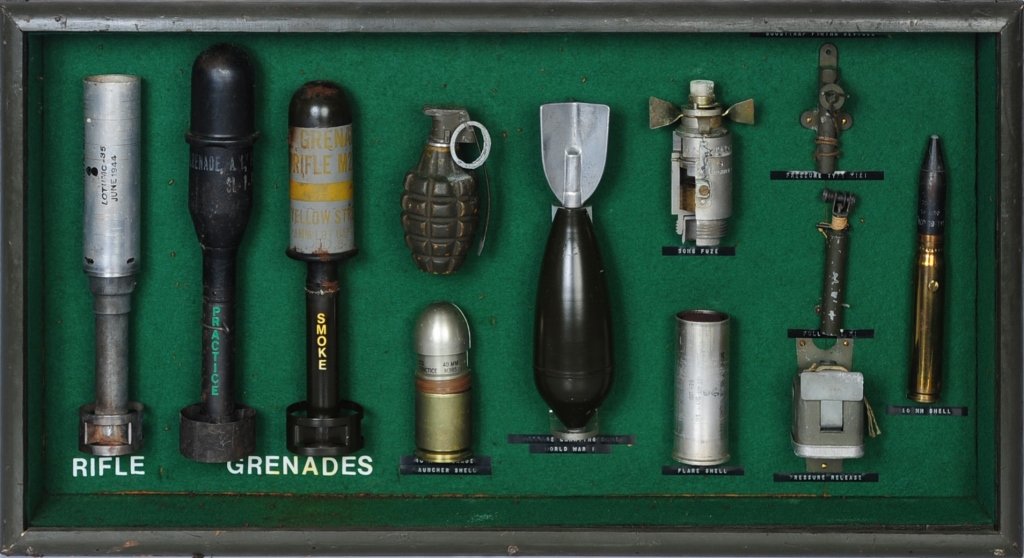 UNIQUE FRAMED WWII US ORDNANCE DISPLAY: Olive drab finish wooden display case with glass front, contains 12 different WWII era examples of battle ordnance to include 20mm round, three different booby trap firing devices which include pressu