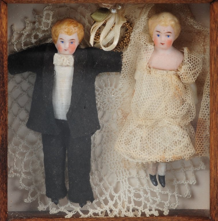 PAIR BISQUE DOLLS IN A SHADOW-BOX FRAME: A pair of bride and groom dolls each measuring 4 inches, framed in a shadow box measuring 6 x 6 inches.