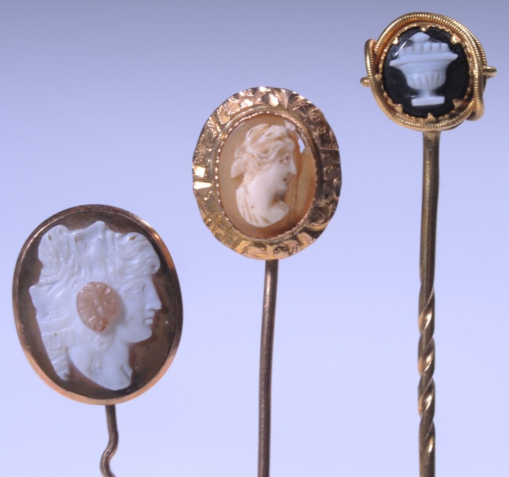 THREE 14KT GOLD CARVED CAMEO STICKPINS: A mourning stickpin with carved onyx urn motif and woven lock of hair in the reverse, inscribed 'L.G. 12 Feb 1837' measures 3.25 inches, weighs 2 grams. Plus two carved hardstone and shell cameos with