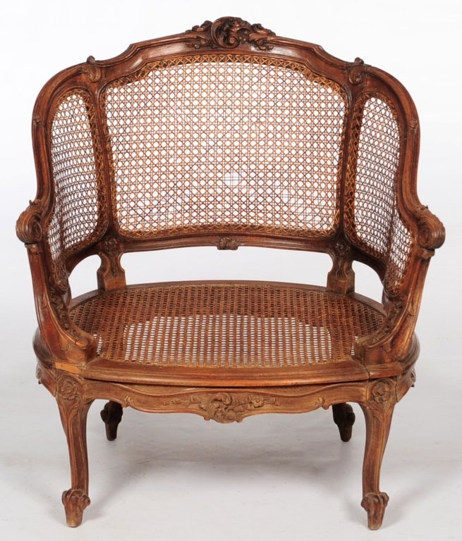 20TH C. CARVED AND CANED BERGERE: Arched leaf-carved caned back with tipped ends continuing to acanthus-carved scrolling arms enclosing caned panels, over oval caned seat, supported on four short cabriole legs headed by a floret and t