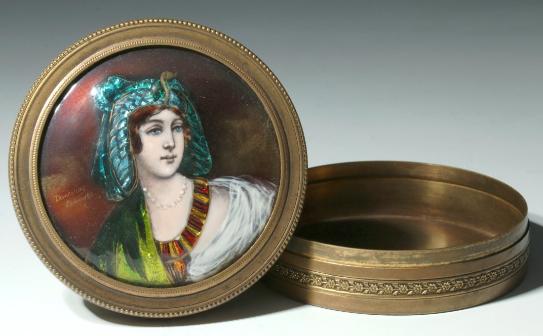 A CIRCA 1900 FRENCH ENAMEL BOX SIGNED DEMEZLIAS LIMOGES: A brass or bronze circular box with cover displaying a French enamel Art Nouveau influence allegorical of an Egyptian queen. Artist signed left hand side. Measures 1.25 x 3.5 inches.