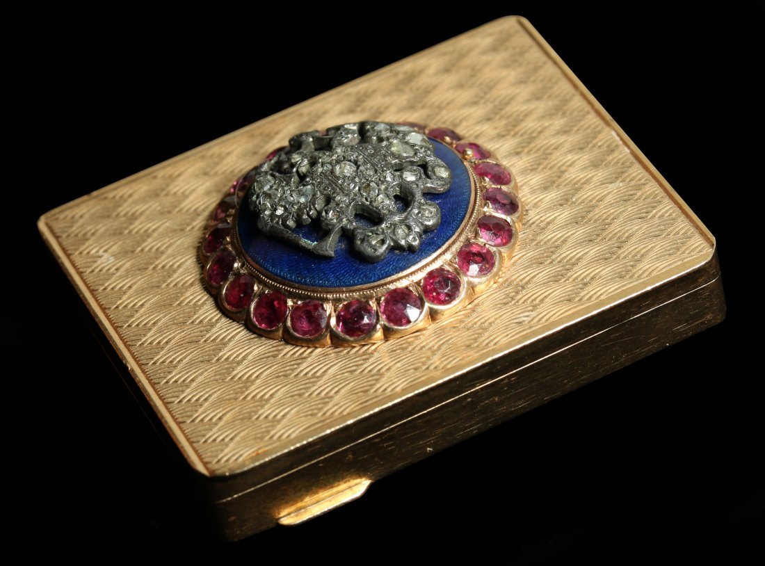 A CIRCA 1900 14K GOLD, DIAMOND AND RUBY SET SNUFF BOX: A rectangular engraved box, the hinged cover set with a double headed eagle on black enamel set with rose cut diamonds and surrounded by faceted ruby-colored stones, stamped mark 14k at the rim, Conti