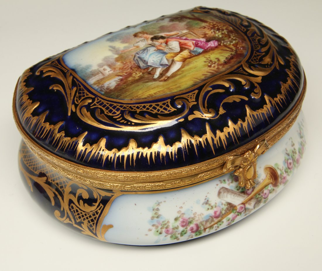 A GOOD SEVRES PORCELAIN BOX ARTIST SIGNED POITEVIN: A circa 1900 hand painted Sevres porcelain box, the demilune shape with hand painted reserves on cobalt blue ground surrounded by raised gilt scrollwork, the convex cover with romantic scene on the li