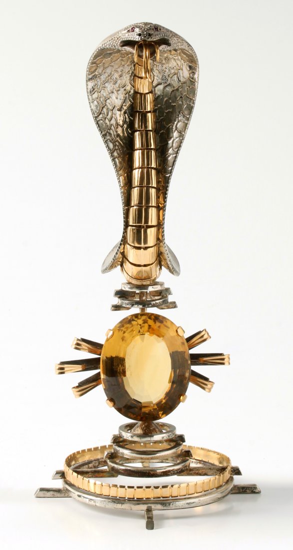 A SILVER AND GOLD COBRA OVERLOOKING A CITRINE SUN: The sterling silver and 10k gold sculpture of a cobra snake with ruby colored gemstone eyes rising over a large citrine quartz faceted gemstone measuring 39 x 32 mm, stands 6.75 inches tall, weight 31