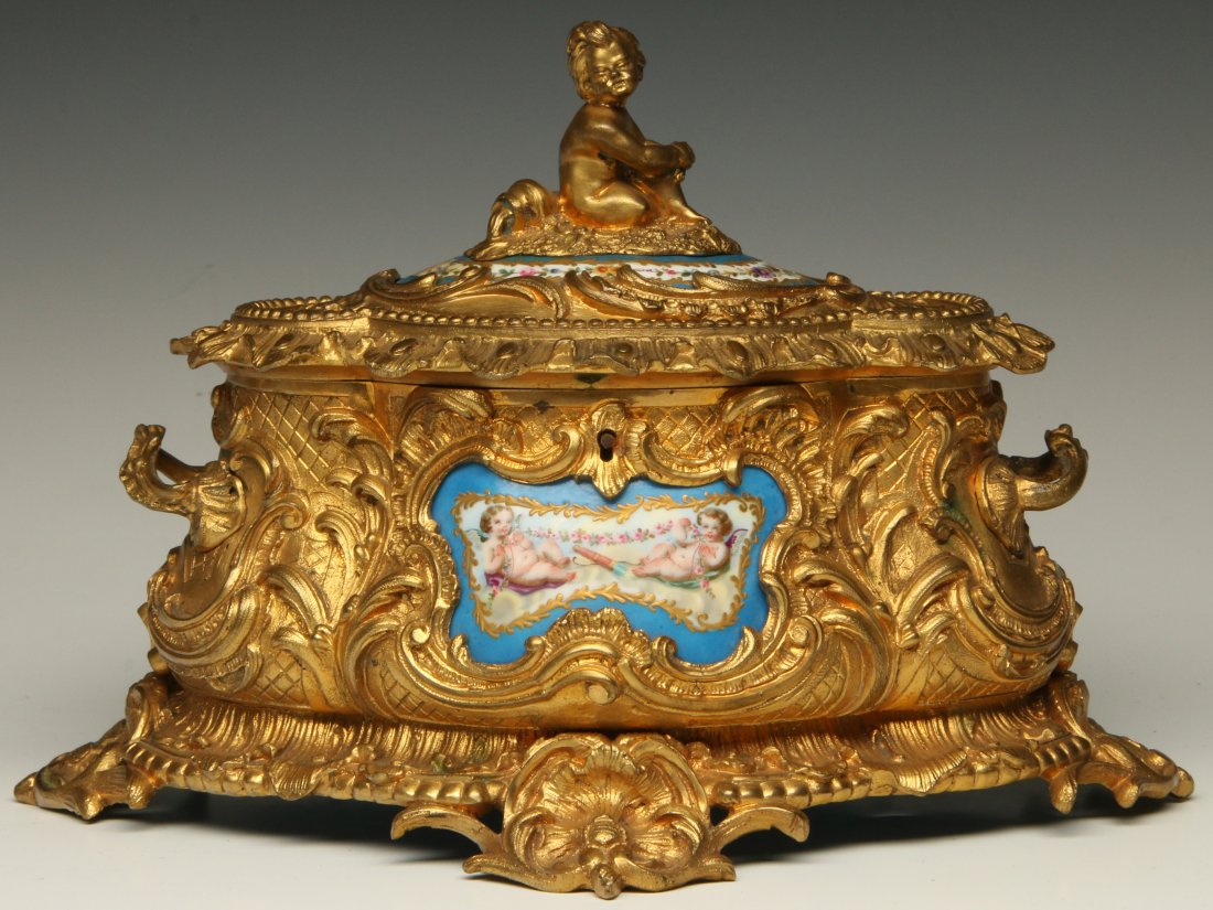 A 19TH C. LOUIS XVI STYLE ORMOLU JEWELRY CASKET: A gilded bronze jewelry casket with predominantly hand painted Sevres type porcelains depicting cherubs and floral garlands. Measures 7 x 10.5 inches.