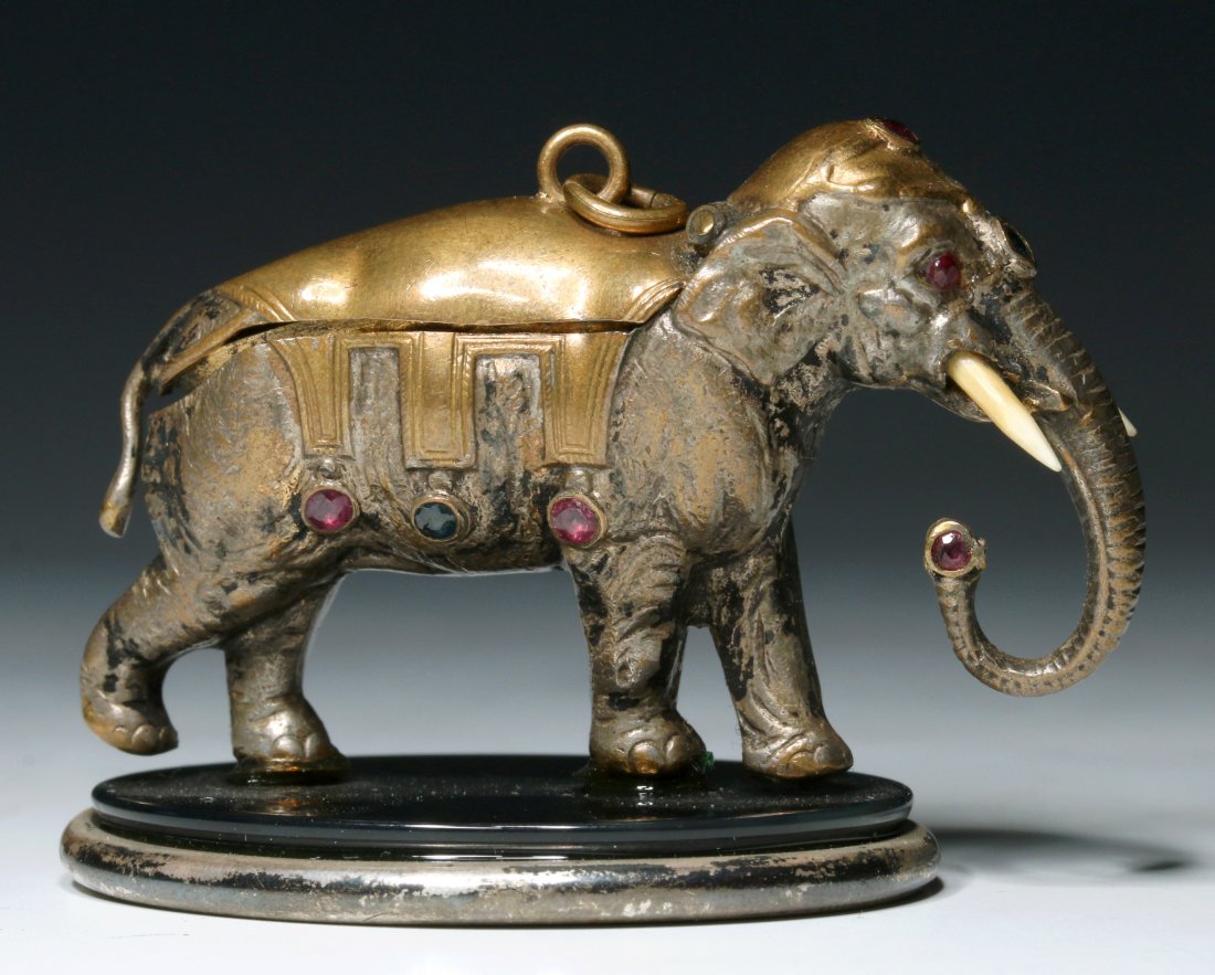 AN EARLY 19TH C. JEWELED ELEPHANT FIGURAL PATCH BOX: A silver plated brass figure with gilt interior, an oval mirror in the hinged cover, ruby eyes, a pair of thin ivory tusks, a jeweled saddle cover and head dress. Measures 1.5 x 2.25 inches. Appears t