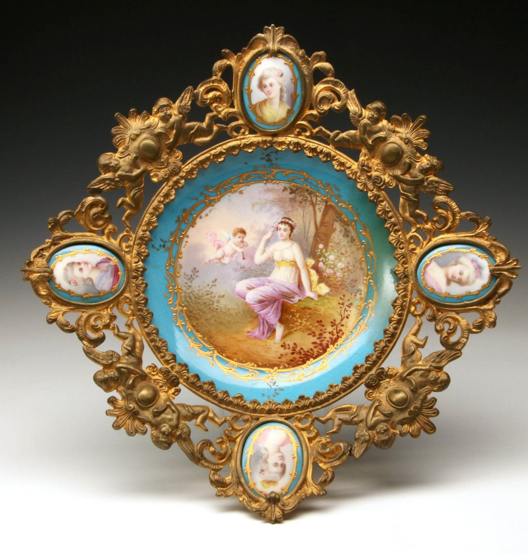 A 19TH C. GILDED BRASS AND SEVRES PORCELAIN CENTERPIECE: The cast openwork frame with porcelain portrait medallions and pairs of cherubs flanking a cartouche, the center a porcelain insert with Sevres factory markings and woodland scene signed F. Lacoste. M