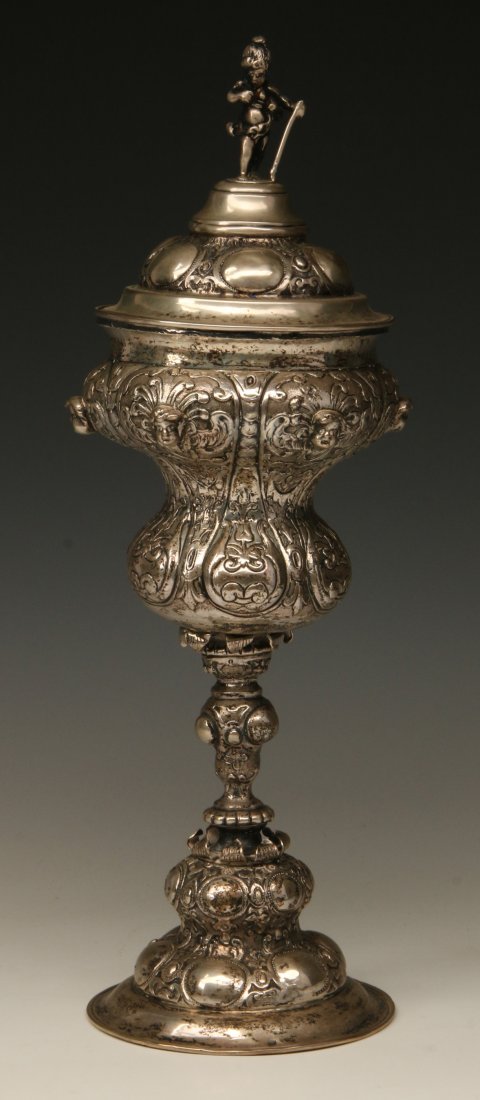 A LATE 19TH C. SILVER COVERED CHALICE ATTR. HANAU: The cover formed by a cast silver dome with child figure and applied hammered rim. A cast silver body with applied hammered rim over three-dimensional cherub faces and relief designs that include fleu