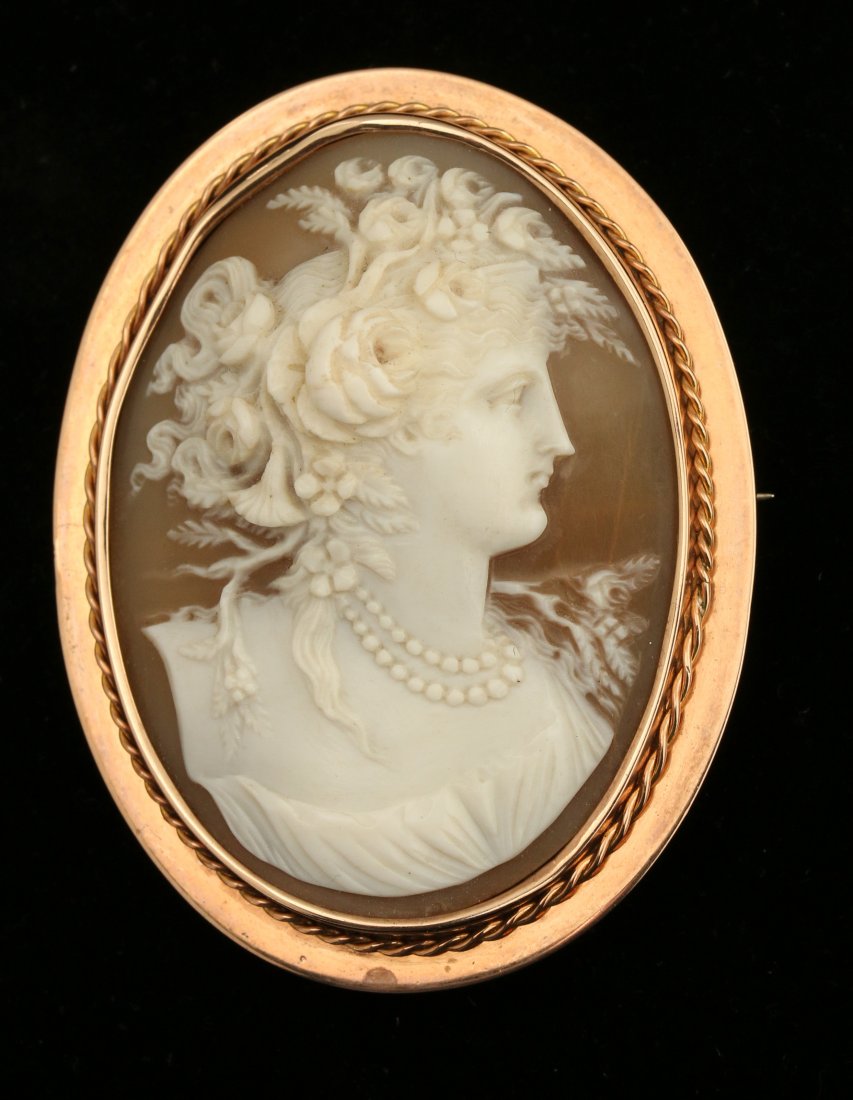 A FINE ANTIQUE HIGH RELIEF CARVED SHELL CAMEO IN 10K: A well carved bust figure adorned with roses in high relief, the bezel encircled by a twisted wire ring. Overall measurement 2.5 x 1.75 inches. Weight of 20 grams. This and 29 other designated lots in