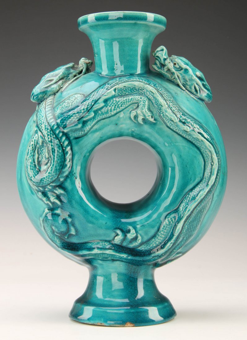 A CHINESE TURQUOISE GLAZED POTTERY VESSEL: A Chinese turquoise glazed circle vase in "bi" disk shape with relief designs of dragons encircling the vessel, 20th century. Measures 8.5 x 4.75 inches.