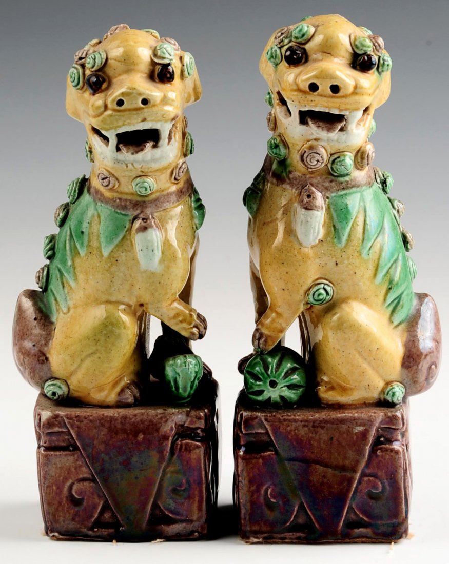 A PAIR OF EARLY 20TH CENTURY GLAZED FOO DOG FIGURES: Chinese pair of biscuit-glazed Fu Dogs atop large aubergine-glazed square stands, yellow bodies with green and aubergine accents; one with paw on a cub and the other with paw atop a ball, 20th century