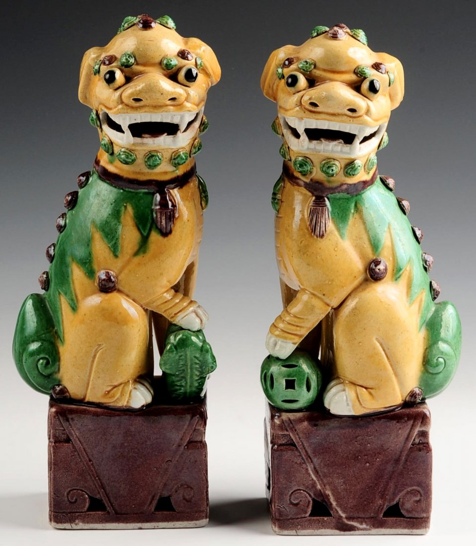 A PAIR OF EARLY 20TH CENTURY GLAZED FOO DOG FIGURES: Chinese pair of biscuit-glazed Fu Dogs atop large aubergine-glazed square stands, yellow bodies with green and aubergine accents, one with paw on a cub and the other with paw atop a ball, 20th century