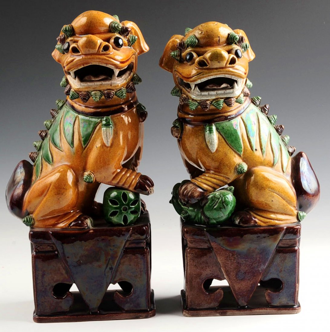 A PAIR OF EARLY 20TH CENTURY GLAZED FOO DOG FIGURES: Chinese pair of biscuit-glazed Fu Dogs; one with paw on a cub and the other with paw atop a ball, yellow bodies with green and aubergine accents atop pierced square aubergine-glazed stands, early 20th