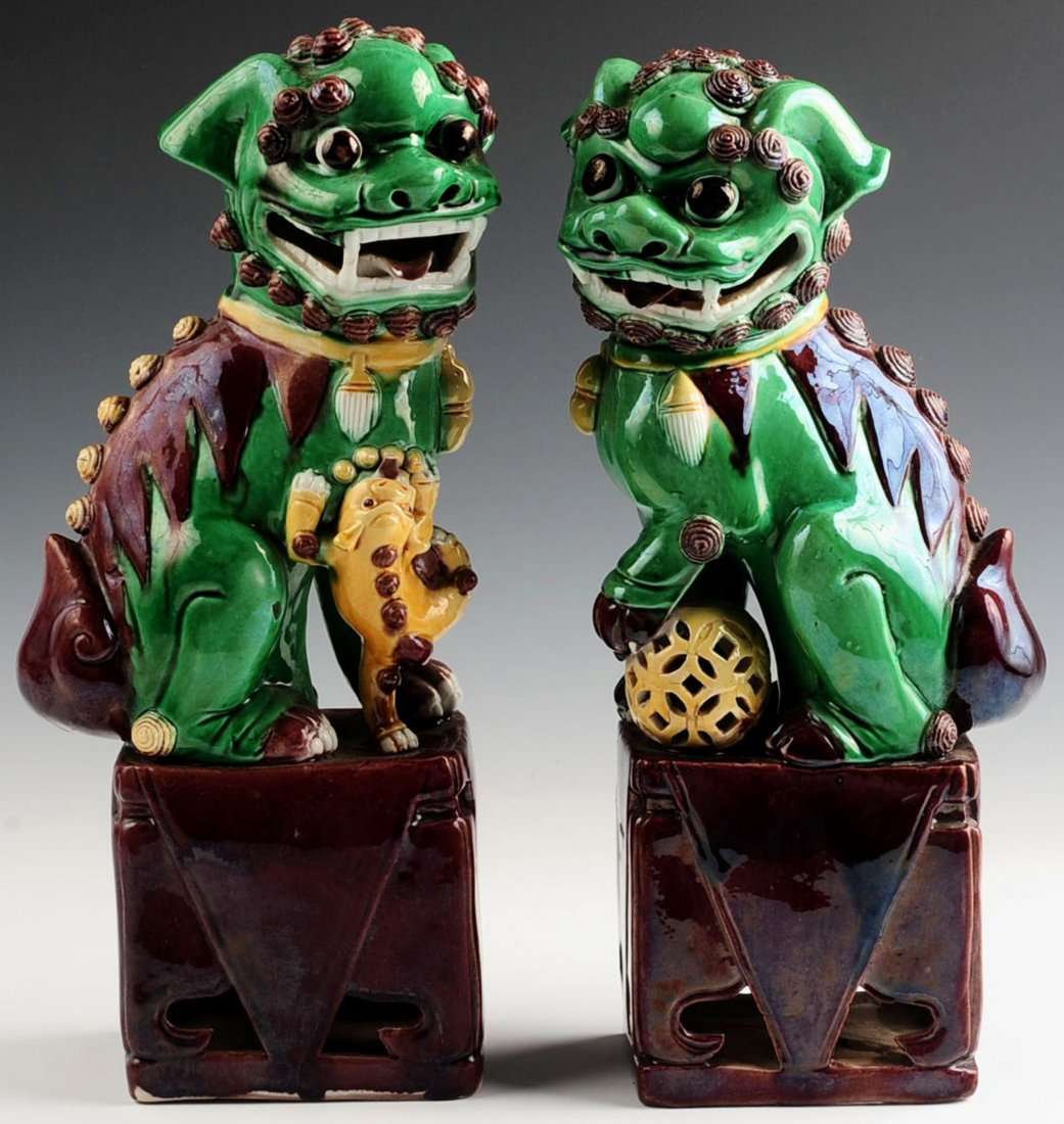 A PAIR OF EARLY 20TH CENTURY GLAZED FOO DOG FIGURES: Chinese pair of biscuit-glazed Fu Dogs; one with paw on a cub and the other with paw atop a ball, green bodies with aubergine and yellow accents, atop pierced square aubergine-glazed stands, early 20t