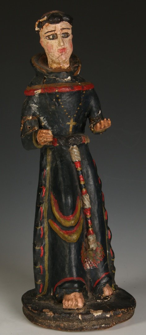 A SPANISH COLONIAL SANTOS OF ST. FRANCIS: Circa 1800, carved and gessoed wood in red, yellow and dark blue black, the barefoot figure with glass eyes wears a robe with cowl and tasseled rope at the waist. Measures 14.5 x 5.5 x 5 inches. Prove