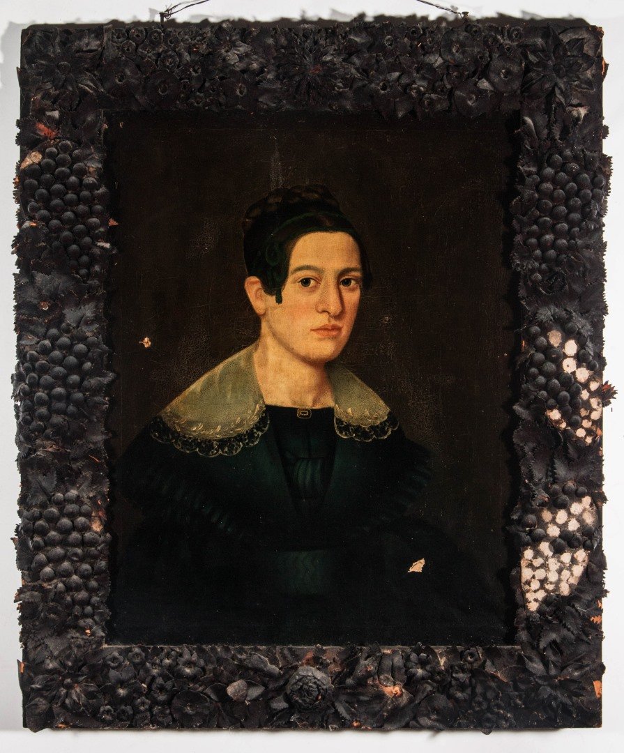 AN EARLY AMERICAN PORTRAIT IN ORIGINAL LEATHER FRAME: An unsigned portrait of an unidentified sitter, a young woman in black dress with a lace collar wearing a gold mourning pin with pearls and memoriam lettering on enamel, her hair woven and worn up wit