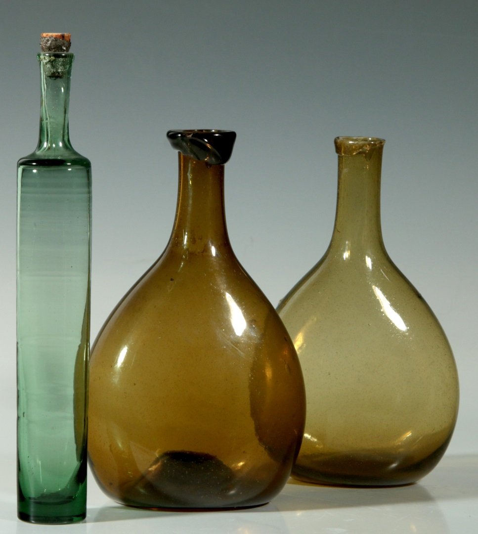 A 19TH C. FREE BLOWN CHESTNUT FLASK, PLUS ANOTHER: A circa 1800 amber chestnut form flask approximately 7 x 4.25 inches with kick-up base and rough pontil, plus a green cylindrical blown spun bottle with plain end and height of 8.25 inches. We ship in