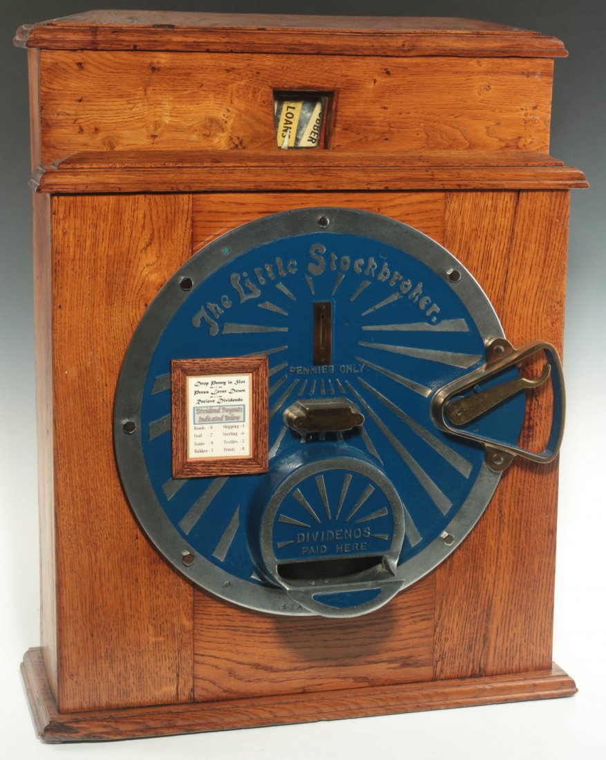 C. 1927 'THE LITTLE STOCKBROKER' COIN OP SLOT MACHINE: An English penny slot machine with a cast aluminum front and oak colored wood case, the investors choices are displayed above and include Rubber, Loans, Trusts, etc. The "Dividends" are paid out below