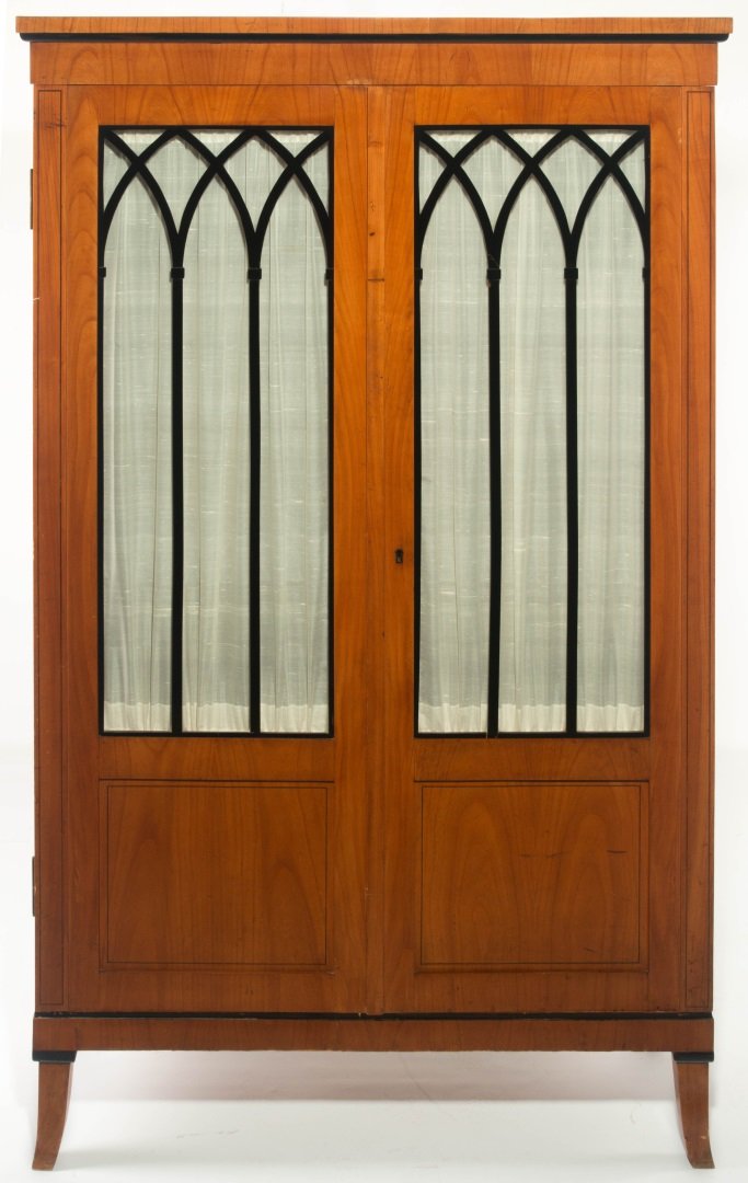 A GOOD LATE 19TH CENTURY BIEDERMEIER TWO DOOR CABINET: A cherry wood Biedermeier style two-door cabinet with ebony trim and door grills; the overhanging top trimmed in ebony above two glazed doors, each with black gothic motif wood lattice inside the glas