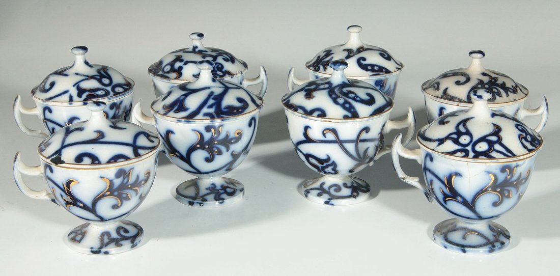 EIGHT 'ROYAL LILY' PATTERN FLOW BLUE COVERED CUPS: Set of eight covered cups, flow blue with gold painted highlights. Measure 3.5 x 3.5 inches overall. We ship in-house for all items with the exception of very large and or very fragile pieces and some