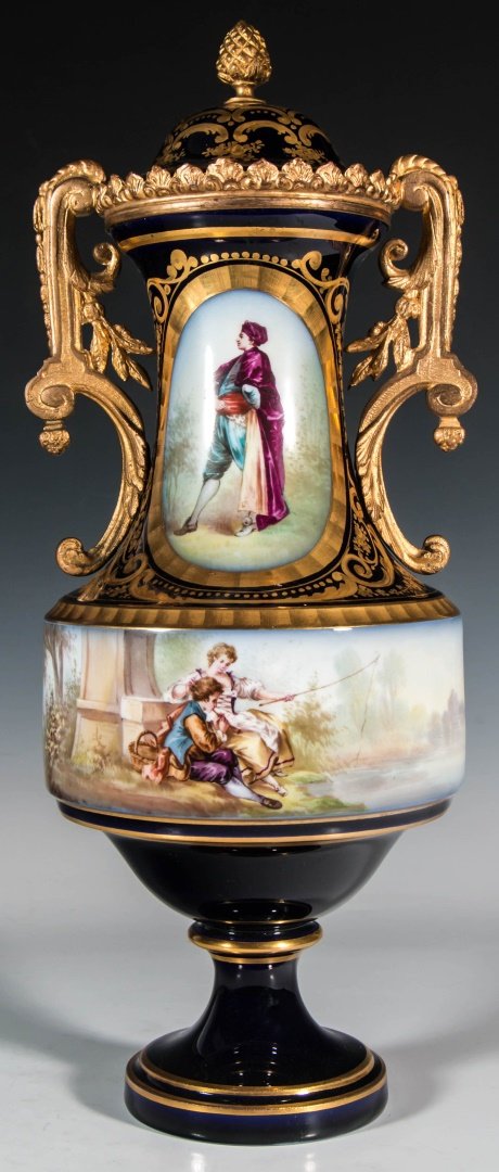 A CIRCA 1900 SEVRES STYLE PORCELAIN COVERED URN: A cobalt ground porcelain vase with oval vertical reserve centering full length portrait one side and floral spray the opposite side; a flat band with hand painted scene of a couple fishing, raised on