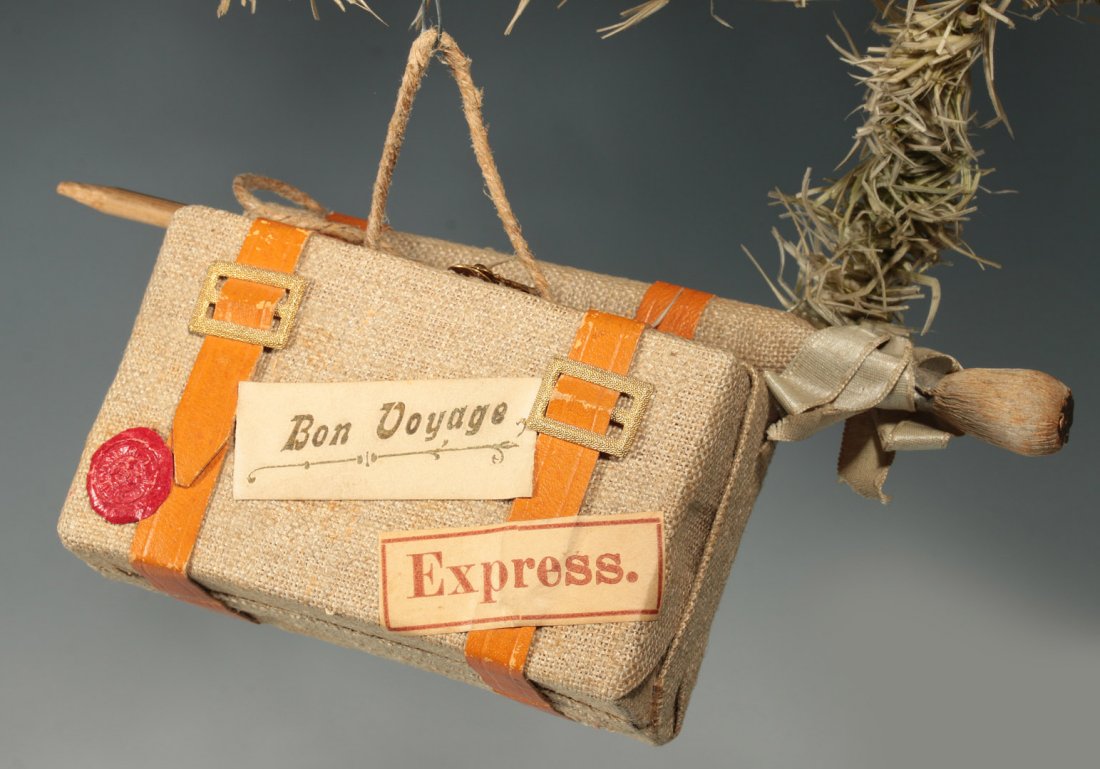CIRCA 1920 CANDY CONTAINER SUITCASE ORNAMENT: Burlap covered cardboard with applied decorative pieces, opens to reveal a lined interior, burlap hinge, measures 3 x 7.5 inches.