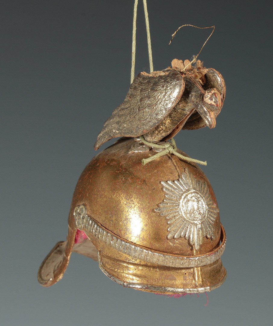 CIRCA 1900 DRESDEN PRUSSIAN HELMET ORNAMENT: A three-dimensional embossed and pieced paper ornament with hand-painted details and a satin lining depicting a Prussian Garde-Kurassier-Regiment featuring parade eagle attachment, measures 2.5 X 2 in