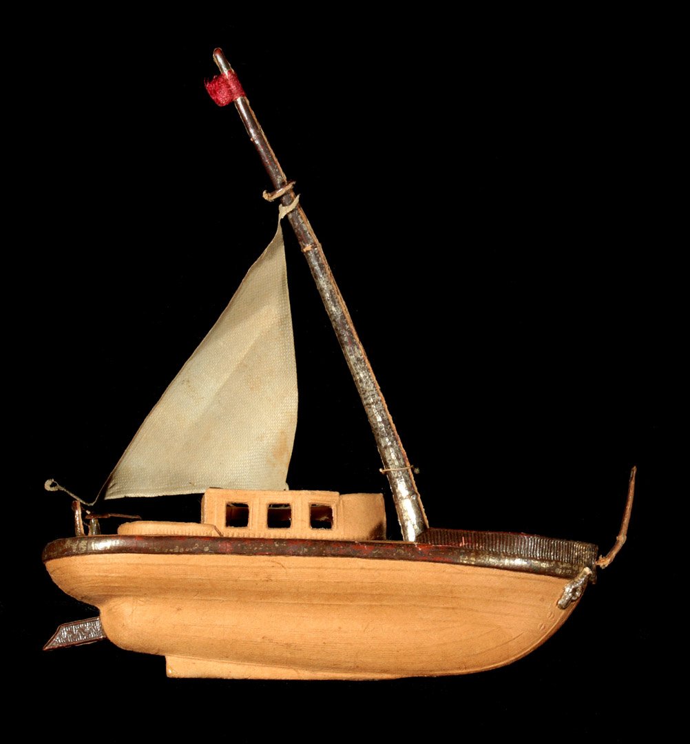 CIRCA 1900 DRESDEN SAILBOAT CHRISTMAS ORNAMENT: A three-dimensional embossed and pieced paper ornament with hand-painted polychrome details and a fabric sail, measures 4 inches to the top of the mast and 4 inches long.