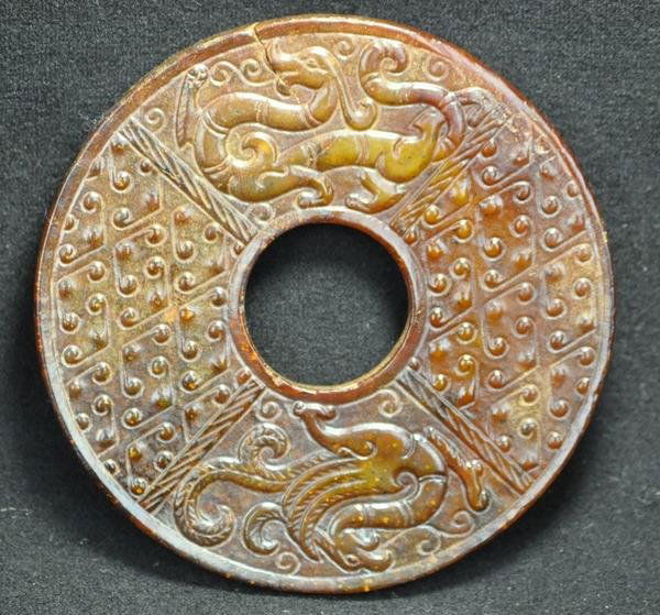 A YELLOW JADE BI.(HAN DYNASTY): Both sides carved with dragons and phoenixs. 3 3/4'' diam Condition report a small hairline crack and natural inclusion