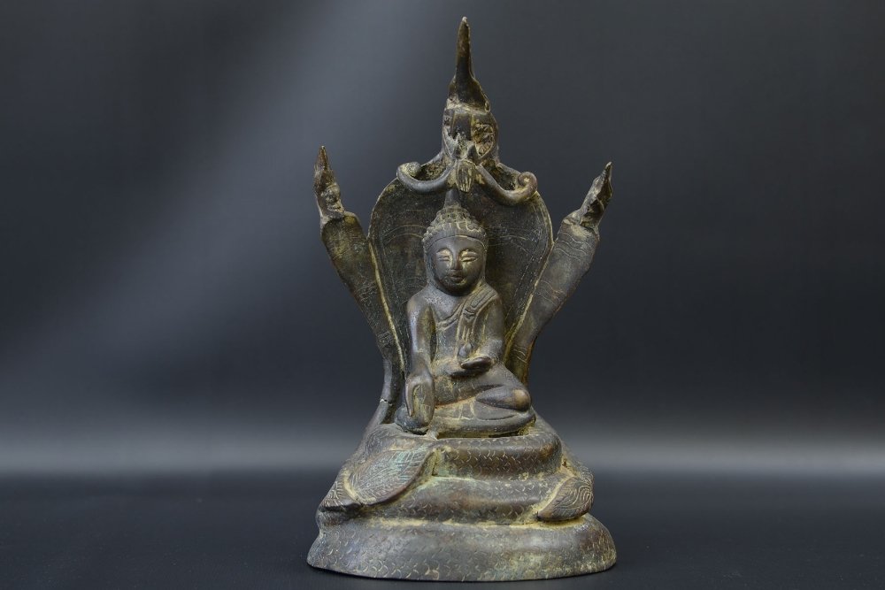 A Cambodian Bronze Buddha with Mucalinda: A Cambodian Bronze Buddha with Mucalinda, the seated Buddha with right hand in varada mudra, the left holding an egg, the Buddha seated on a throne likely formed by Mucalinda, appx. 9 in. H. Provenanc