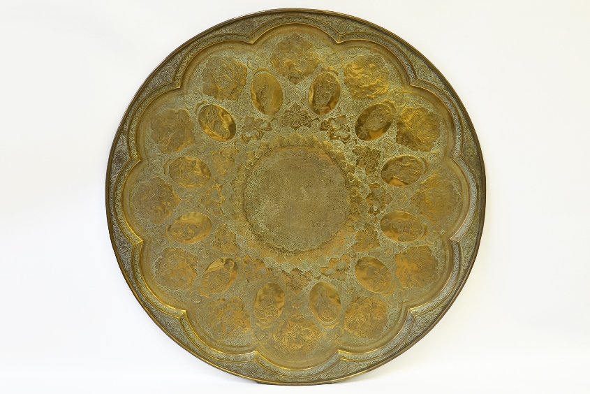 A Large Persian Engraved Brass Charger: A Large Persian Engraved Brass Charger, with scalloped edges, engraved with 12 medallions depicting men of high standing and 12 scenes from daily life, with green patina, appx. 38 7/8 in. DIA.