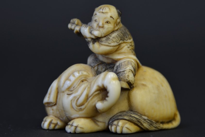 A Japanese Ivory Netsuke, Edo Period: A Japanese Ivory Netsuke, Edo Period, in the form of a flute player seated on a recumbent elephant, appx. 1 3/8 in. W.