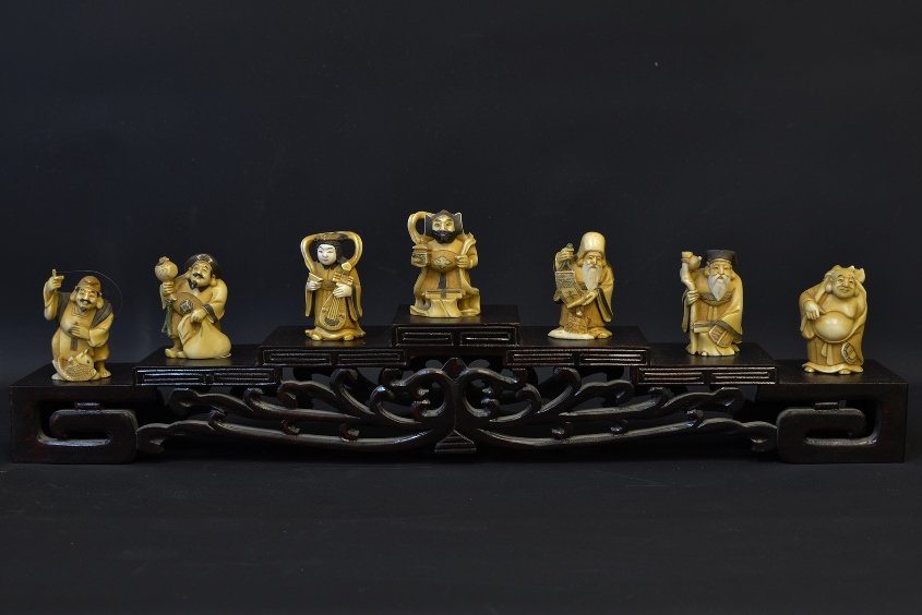 A Japanese Ivory Set, Seven Gods of Fortune: A Japanese Ivory Set, Seven Gods of Fortune, late 19th century, including carved figures of Ebisu, Daikoku, Benten, Bishamon, Fukurokujin, Jurojin, and Hotei, with tiered wood display stand, the talle