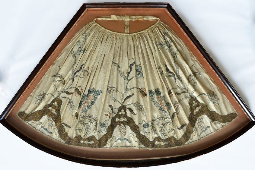 A Chinese Silk Embroidered Apron: A Chinese Silk Embroidered Apron, the apron embroidered with flora and rockwork, in fan shaped shadow box, appx. 49 1/2 in. W, 24 3/4 in. W.