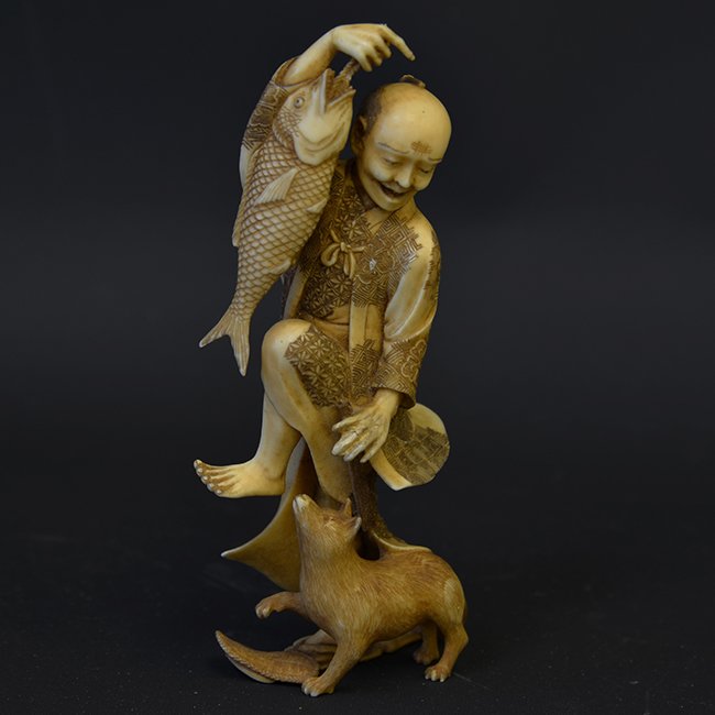 Japanese Meiji Period Ivory Figure: Japanese Meiji Period Ivory Figure, the statue of a man holding a fish in his right hand as he fends off a hungry cat at his right foot, with a small chip to the rope top, a finger on his left hand re