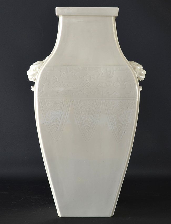 A Chinese Blanc de Chine Porcelain Vase: A Chinese Blanc de Chine Porcelain Vase, with square everted mouth rim, the body incised with archaic type taotie masks above lappets, mounted to the side with mask heads, appx. 14 1/8 in. H.