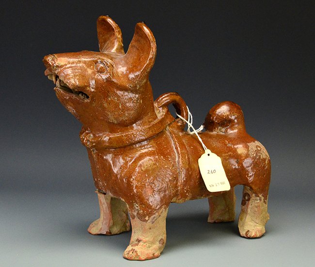 A Chinese Glazed Red Earthenware Dog, Han Dynasty: A Chinese Glazed Red Earthenware Dog, Han Dynasty, the animal standing and facing forward with mouth open and ears raised, wearing a harness, his tail curled over his back, appx. 10 1/4 in. H, 10 1/2